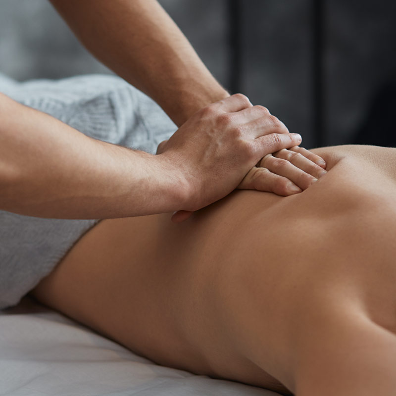 Young handsome man enjoying a back massage. Professional massage therapist is treating a male patient in apartment. Relaxation, beauty, body and face treatment concept. Home massage.