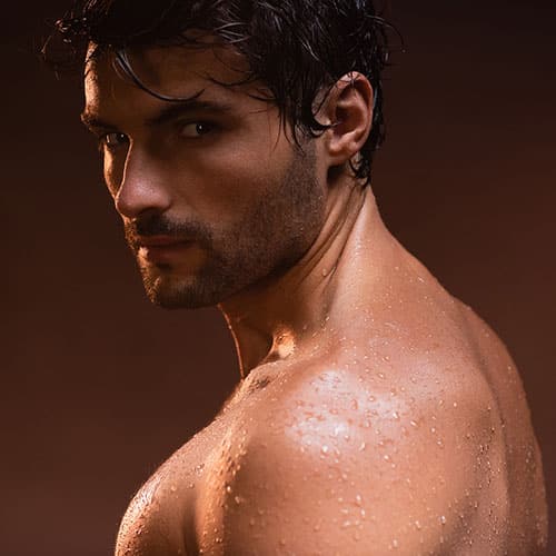 wet, sexy man looking at camera while posing on dark background