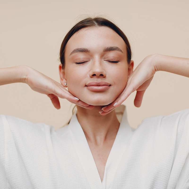 Woman in white bathrobe doing a facial massage, eyes closed. Woman in white bathrobe doing a facial massage, eyes closed.